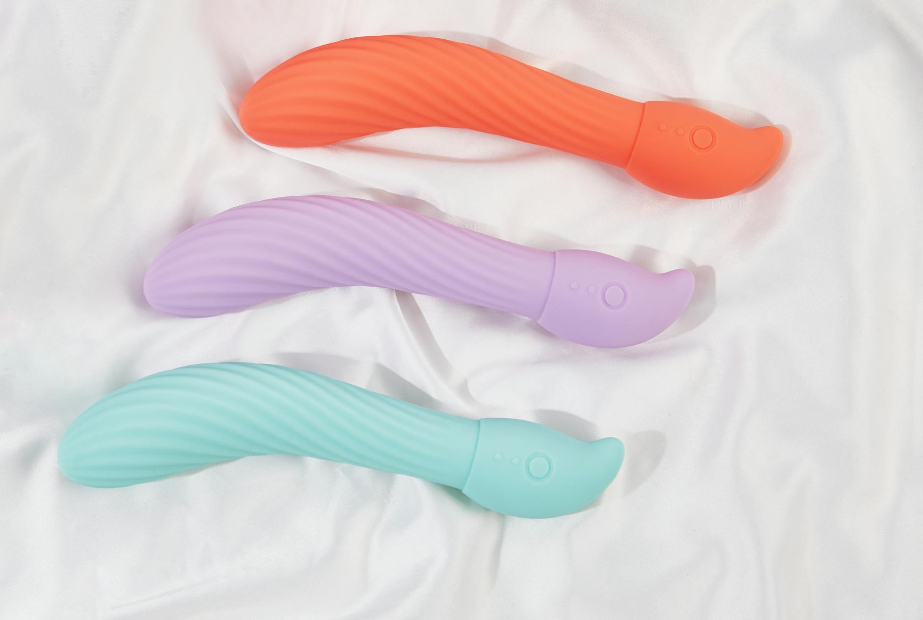 Three colorful vibrators arranged on white fabric, showcasing different textures and designs