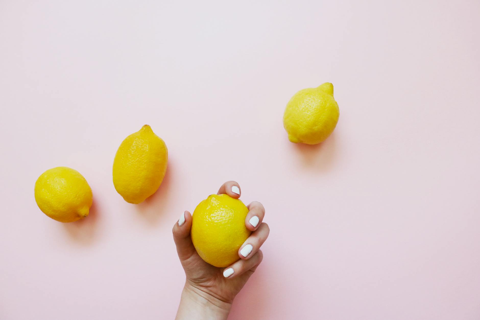 A hand holding a fresh lemon on a soft pink background, symbolizing natural pleasure and restoration.