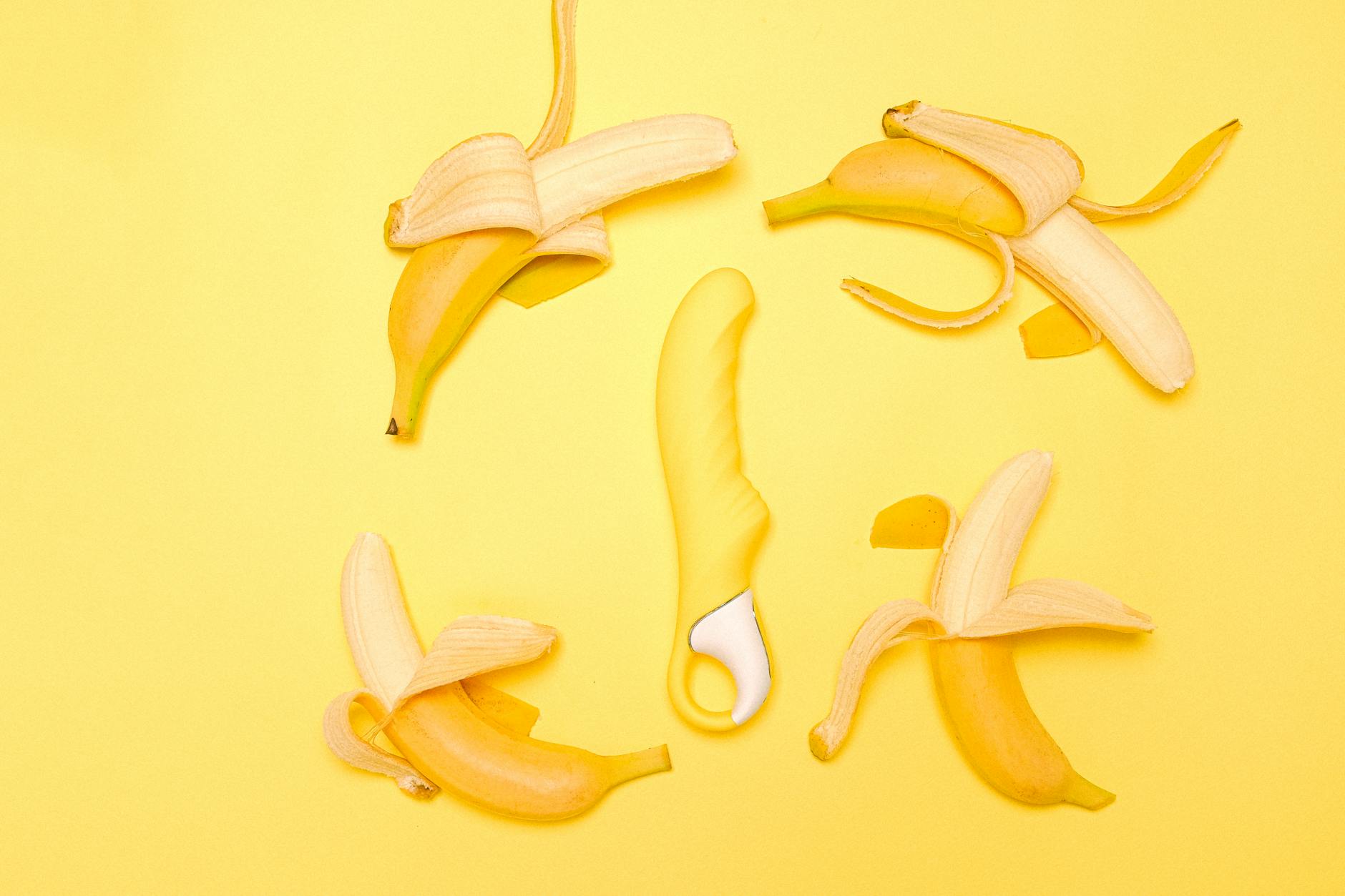 Bright yellow lemon vibrator on a minimalist surface with fresh lemons, showing the toy's curved design