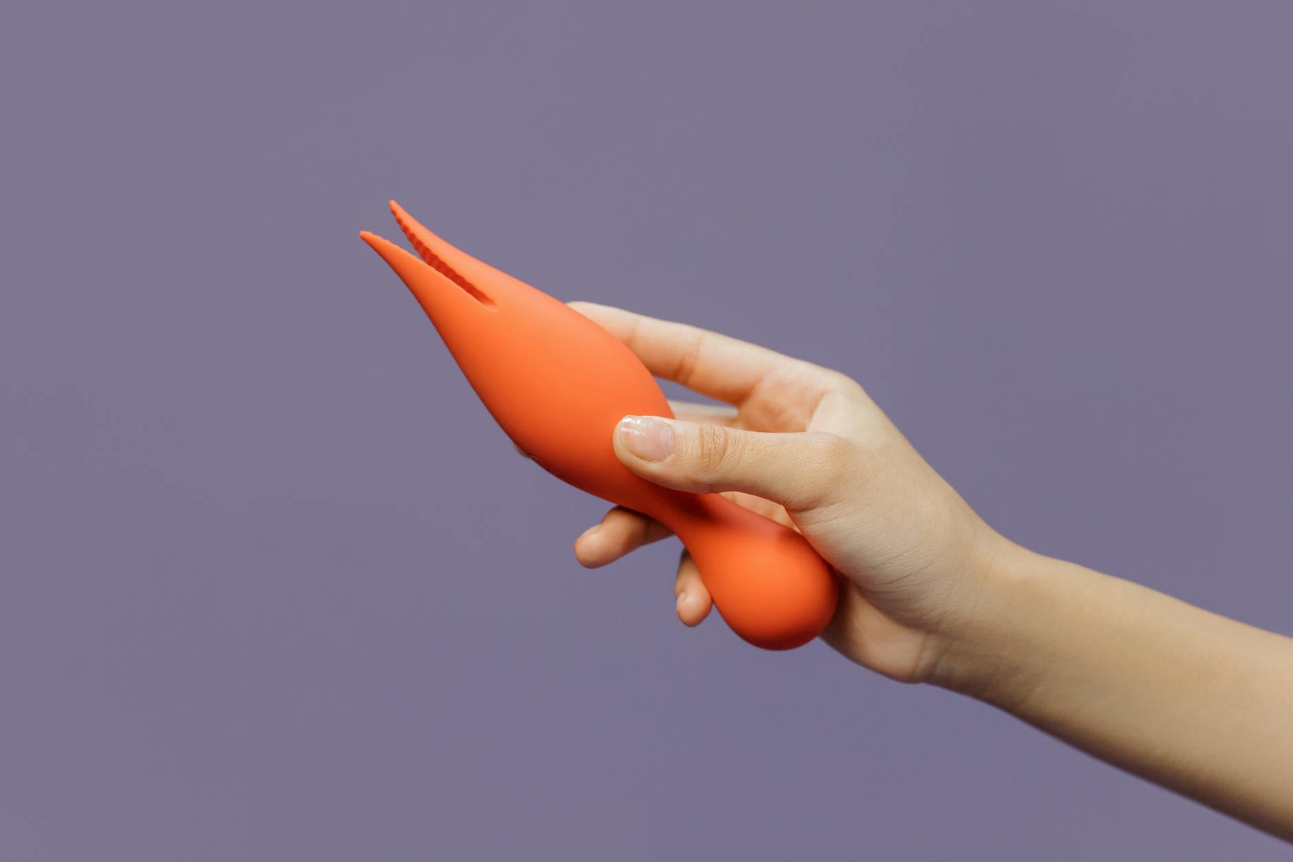 A hand holding a lemon clitoral vibrator against a minimalistic purple backdrop, showcasing modern sensuality and intentional pleasure.