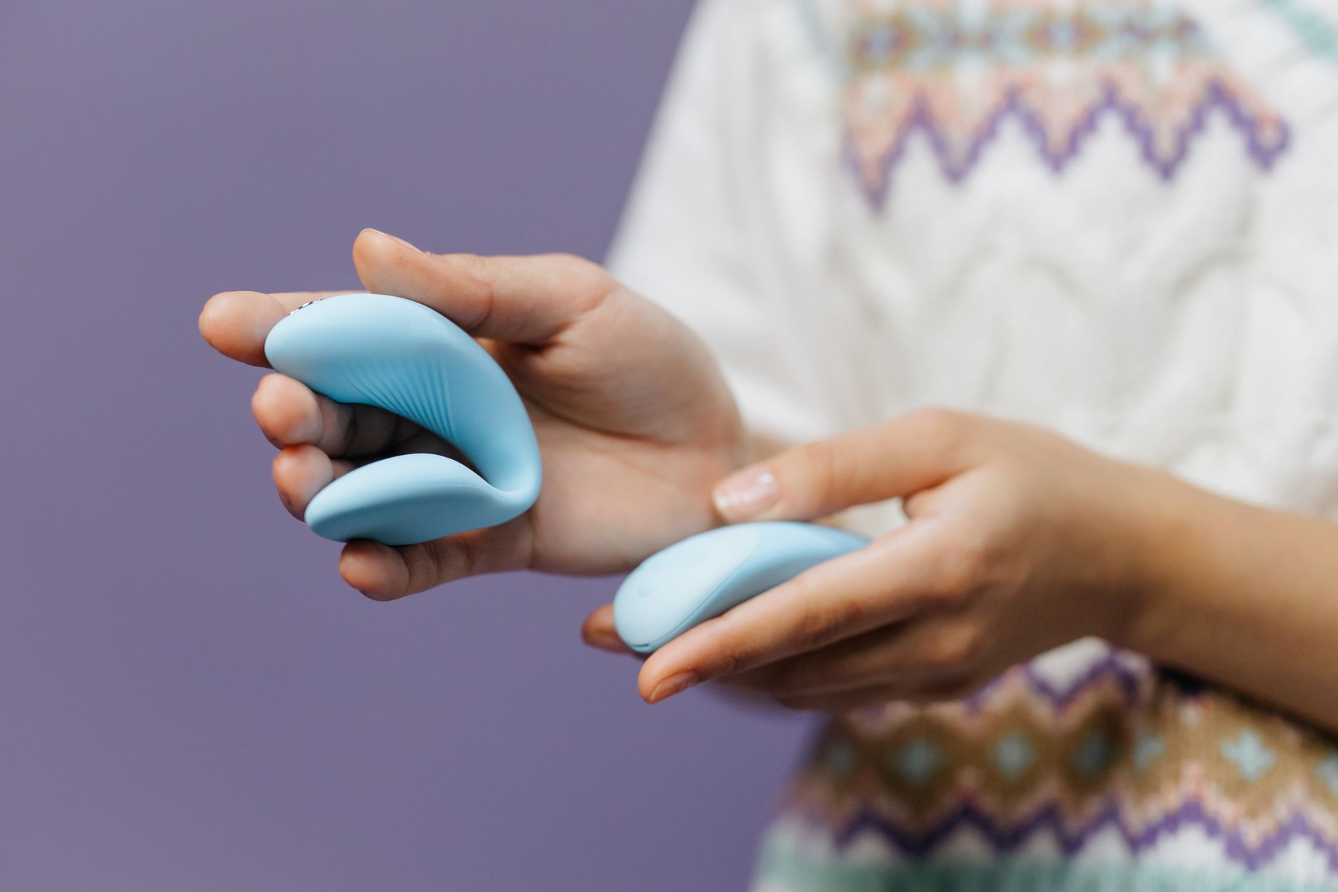 Close-up of hands holding a sleek lemon clitoral vibrator against a textured background