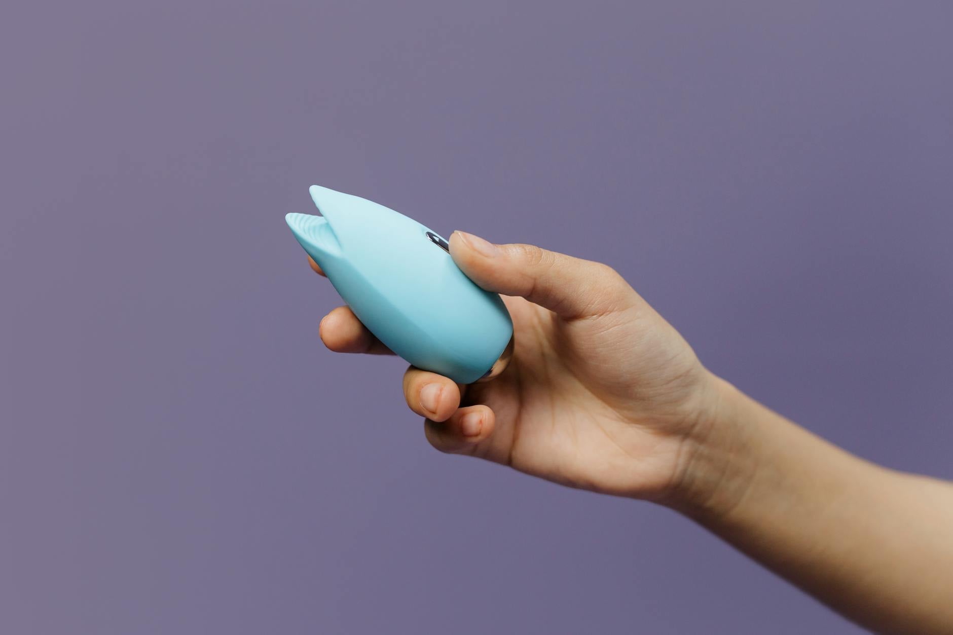 A blue silicone clitoral vibrator held in hand against a purple background, promoting shared exploration and intimacy
