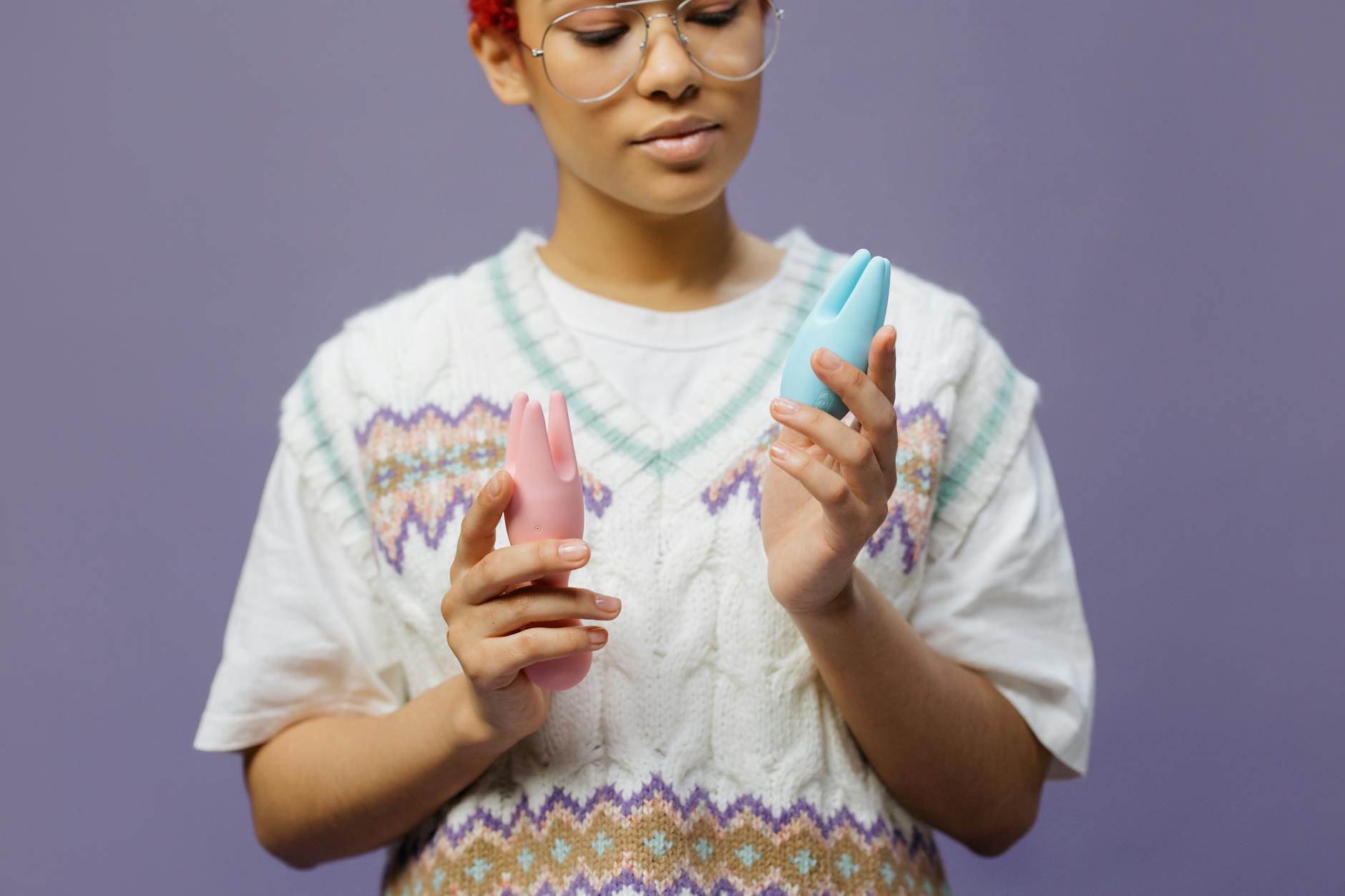 Woman holding blue and pink silicone clitoral vibrators, examining options for sensitive skin care